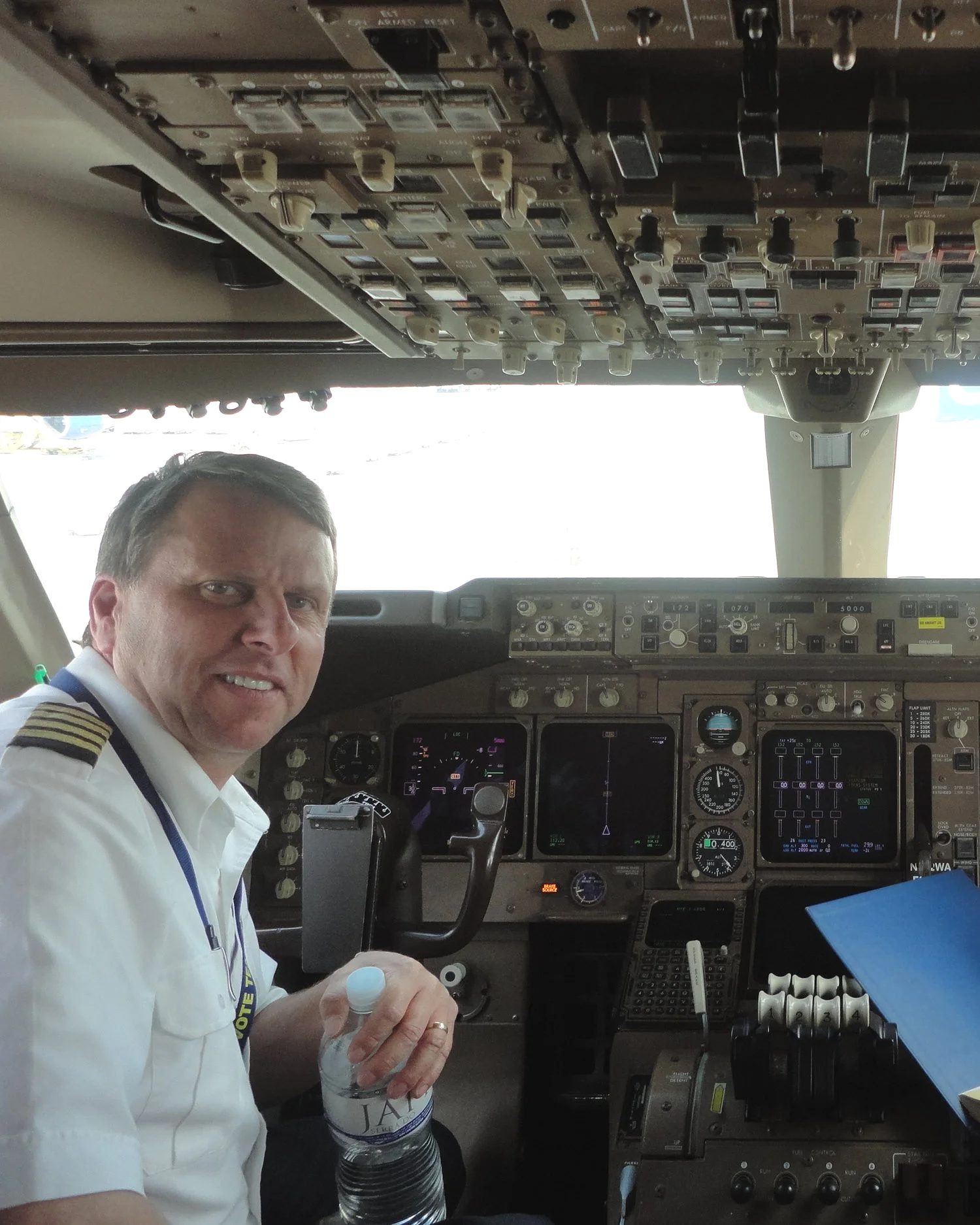 A pilot in uniform smiling from the seat of an airliner cockpit