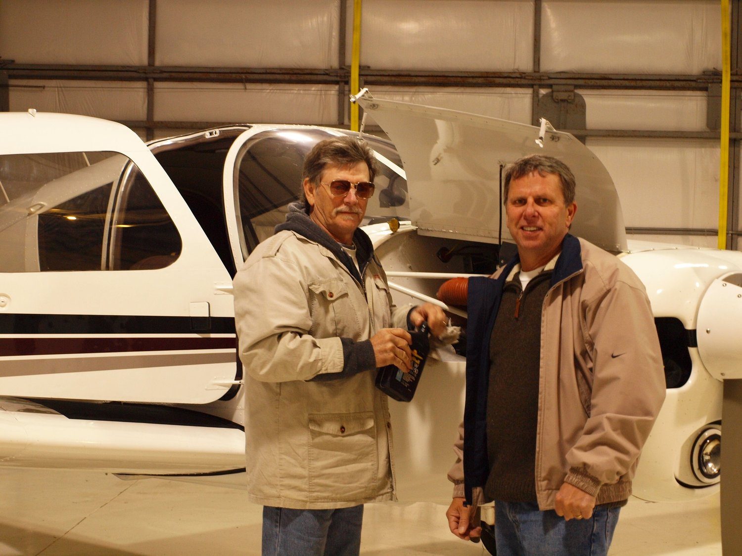 Two men standing beside a small airplane in a hangar