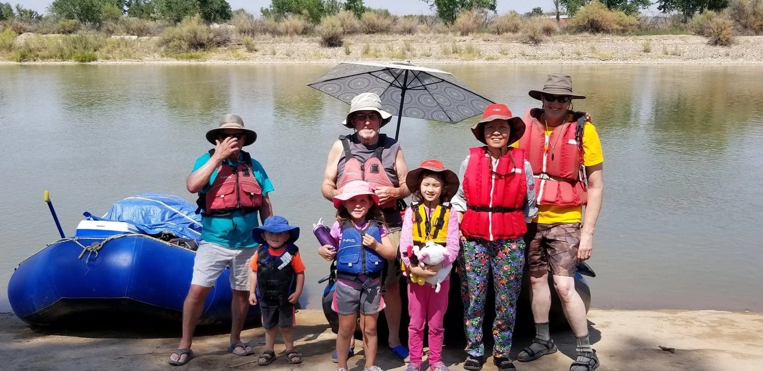 A family in life jackets lined up beside a river raft