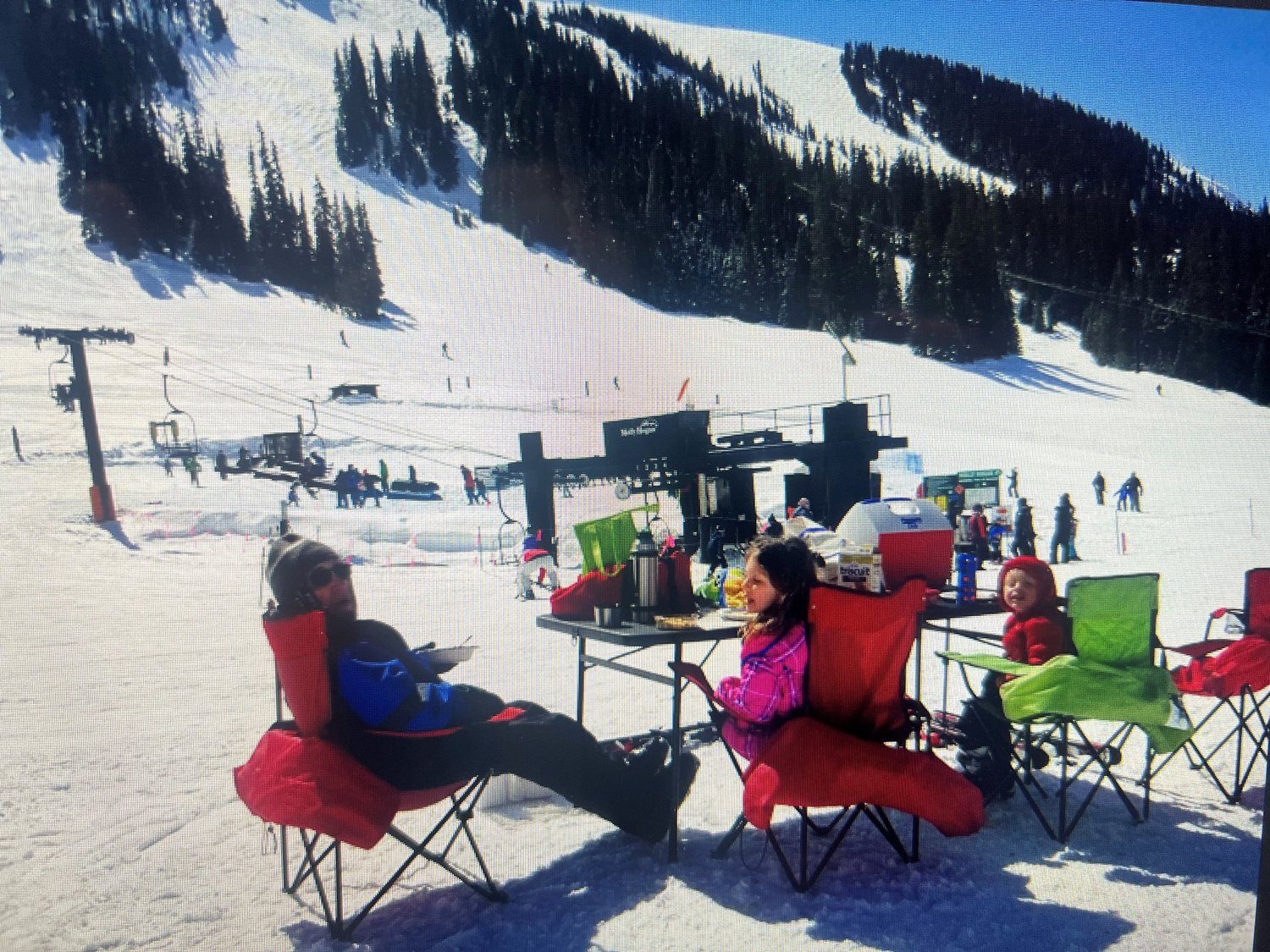 Skiers relaxing in camp chairs at the base of a ski hill